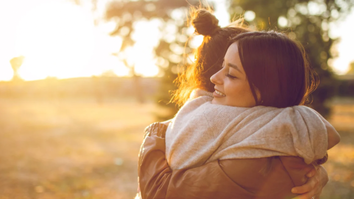 Auf dem Bild sieht man zwei Frauen, die sich im warmen Abendlicht umarmen